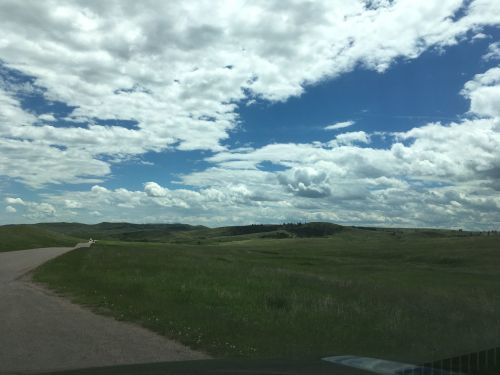 A scenic view of rolling green hills under a partly cloudy blue sky, with a winding road in the foreground.