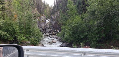A scenic view of a waterfall cascading through rocky terrain, surrounded by lush green trees.