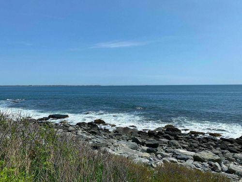 A serene coastal view featuring rocky shores and gentle waves under a clear blue sky.