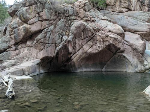 Rocky terrain with smooth, large boulders surrounding a calm, clear pool of water.