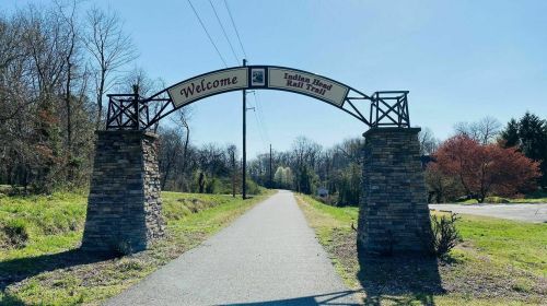 Welcome archway at the Indian Head Rail Trail, with a clear path and trees in the background on a sunny day.
