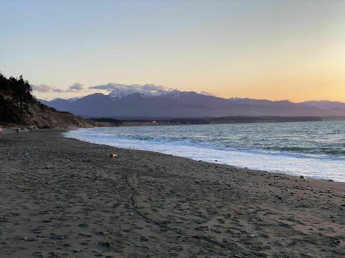 A serene beach at sunset, with gentle waves and mountains in the background under a colorful sky.