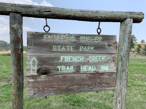 Wooden sign for Custer State Park, indicating the French Creek Trail Head is 9 miles ahead.