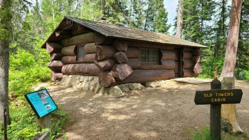 A rustic log cabin surrounded by trees, with a sign reading "Old Timers Cabin" nearby.