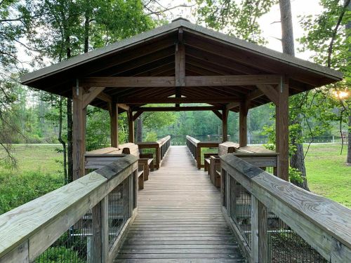 A wooden gazebo with a walkway leading to a serene, green landscape and a body of water in the background.
