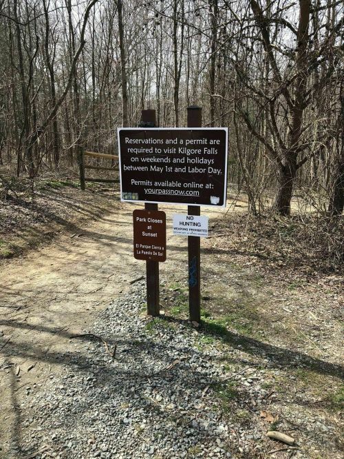 Sign at a trailhead indicating permit requirements for Kilgore Falls, with park hours and no hunting notice.