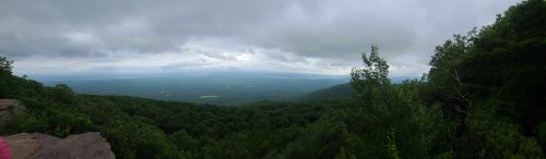 Panoramic view of a lush green landscape under a cloudy sky, with distant hills and a body of water visible.