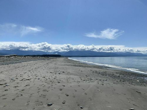 A serene beach scene with footprints in the sand, mountains in the distance, and a clear blue sky.