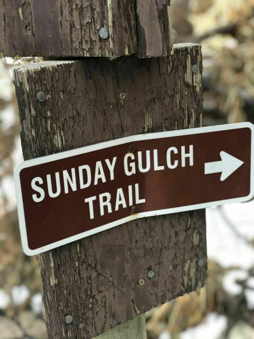 A weathered wooden sign pointing right, labeled "Sunday Gulch Trail."