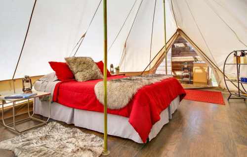 Cozy glamping tent interior with a red bedspread, fur accents, and wooden decor, featuring a warm, inviting atmosphere.