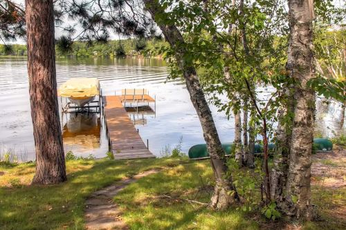 A serene lakeside scene with a wooden dock, a boat covered with a tarp, and lush greenery surrounding the water.