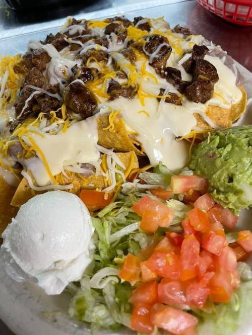 A plate of nachos topped with cheese, beef, and served with guacamole, lettuce, and diced tomatoes.