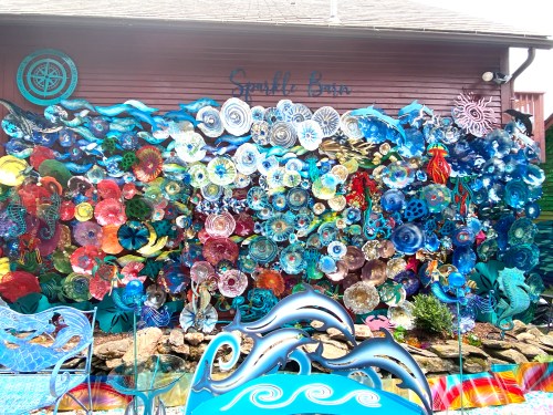 A vibrant mural of colorful sea-themed art made from various materials, displayed on a wall outside a building.