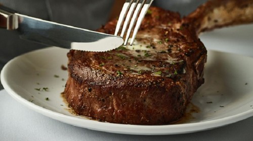 A close-up of a juicy steak on a plate, with a knife and fork poised to cut into it.