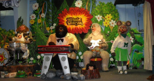 A colorful stage with animatronic animals performing music, featuring a gorilla, a yeti, and a mouse in costumes.