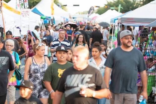 A busy street fair with diverse crowds, colorful tents, and vendors, showcasing a lively community atmosphere.