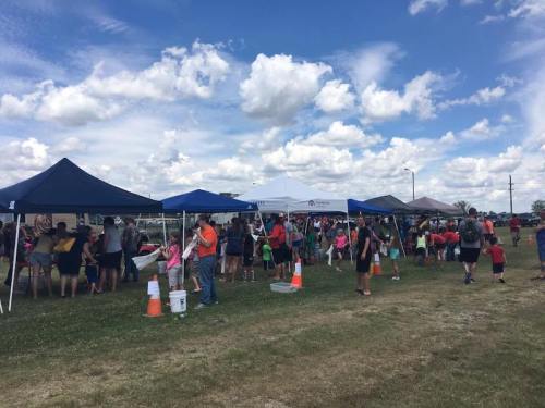 A crowd gathers under tents at an outdoor event, with people mingling and enjoying activities on a sunny day.