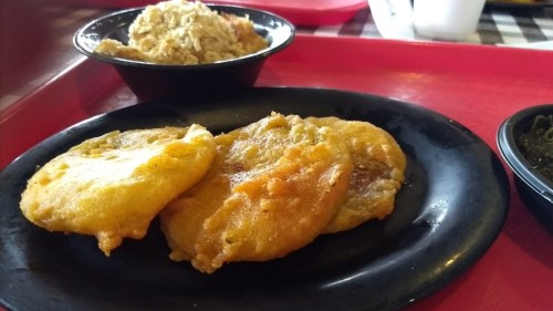 Three golden fried patties on a black plate, with a side of coleslaw in a small bowl. Red tray background.