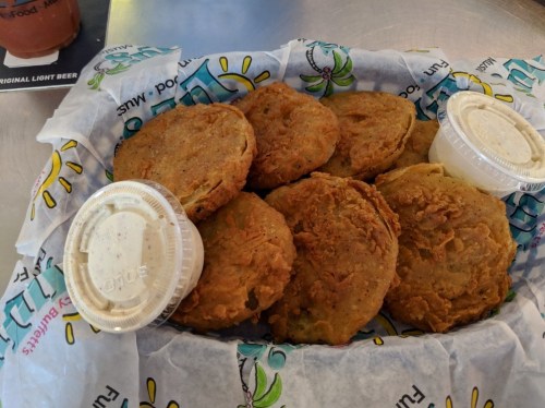 A basket of golden-brown fried green tomatoes with two cups of dipping sauce on the side.