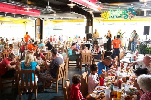 A lively restaurant scene with diners enjoying meals, a band performing, and colorful decor in a vibrant atmosphere.