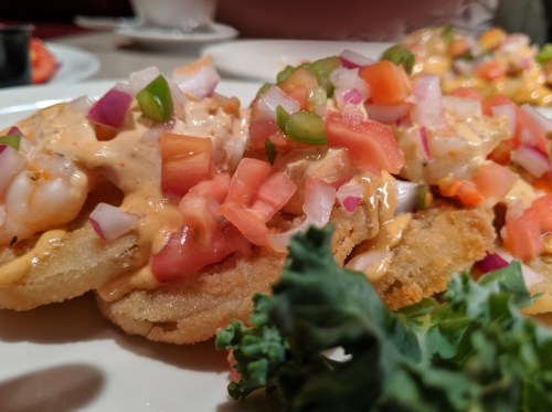 A close-up of fried shrimp topped with diced tomatoes, onions, and green peppers, garnished with kale.