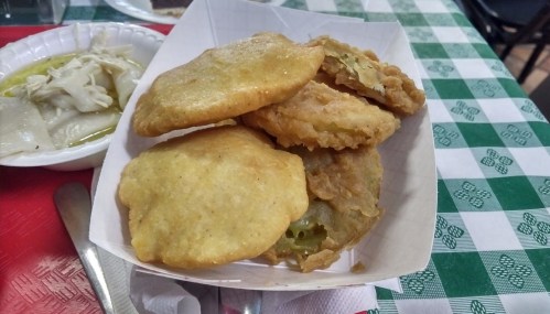 A basket of golden, crispy fried snacks, including stuffed pastries, on a checkered tablecloth.