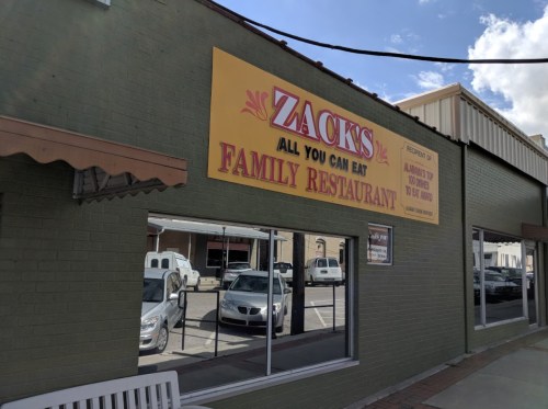 Exterior of Zack's All You Can Eat Family Restaurant, featuring a large sign and windows reflecting nearby cars.