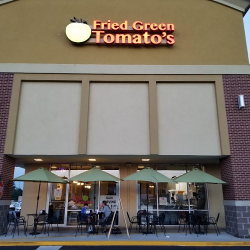 Exterior of Fried Green Tomato's restaurant with outdoor seating and green umbrellas, illuminated sign above.