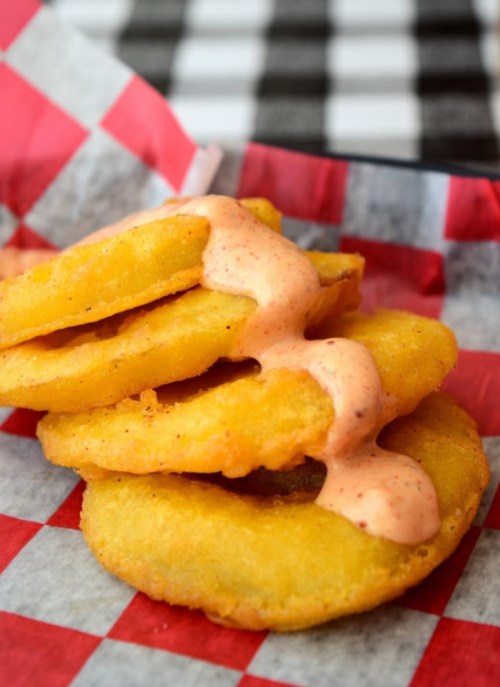 A stack of golden fried patties drizzled with a creamy sauce, served in a red and white checkered basket.