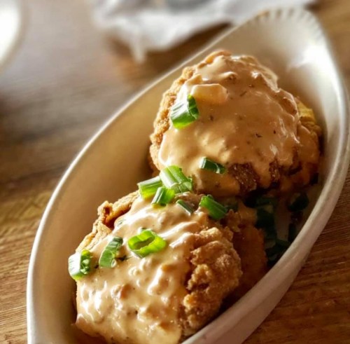 Two crispy fried patties topped with creamy sauce and green onions, served in a white dish.
