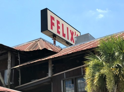 Sign for "Felix's" on a building with a rusted roof and palm trees under a clear blue sky.