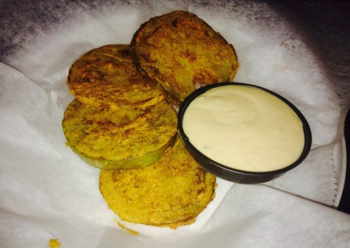 Fried green tomatoes served with a creamy dipping sauce on a white paper-lined plate.
