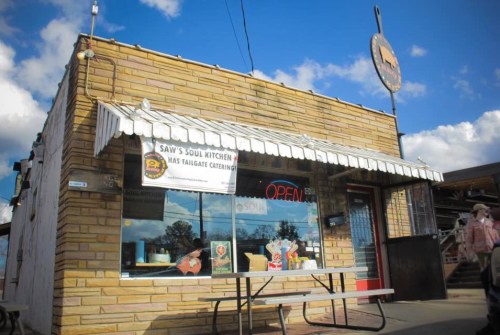 A small, stone building with a striped awning and an "Open" sign, featuring a picnic table outside.