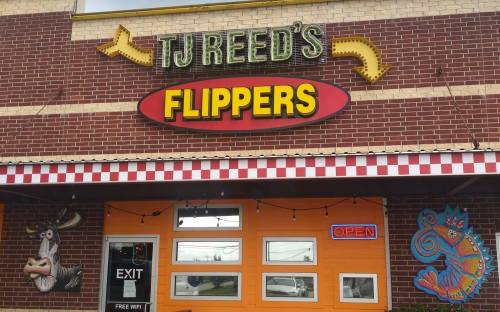 Sign for "TJ Reed's Flippers" with colorful decorations and an "OPEN" sign on a brick building.