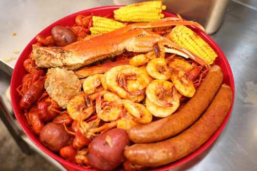 A large red platter filled with seafood, including crab, shrimp, crawfish, corn, potatoes, and sausage.