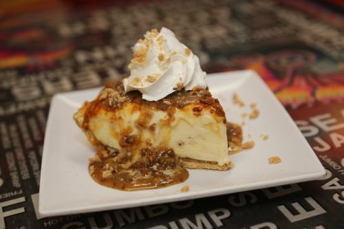 A slice of cheesecake topped with whipped cream and caramel sauce, served on a white plate.
