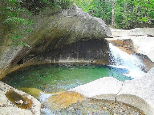 A serene natural pool with clear green water, surrounded by smooth rock formations and a small waterfall.