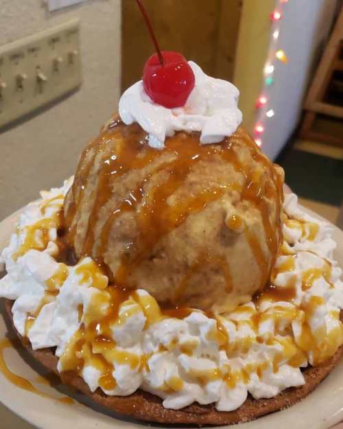 A large ice cream sundae topped with whipped cream, a cherry, and caramel sauce, served on a plate.