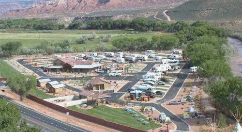 Aerial view of a campground with RVs, tents, and a main building, surrounded by greenery and mountains.