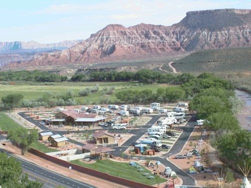 Aerial view of a campground with RVs, surrounded by mountains and greenery, near a river.