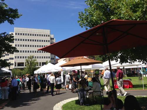 A bustling outdoor market with tents, people mingling, and a clear blue sky in the background.