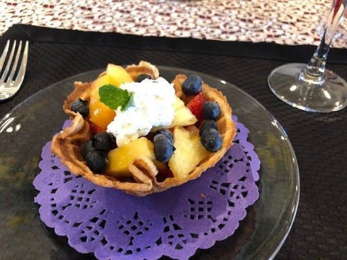 A fruit tart with a crispy shell, filled with assorted fruits and topped with whipped cream, on a purple doily.