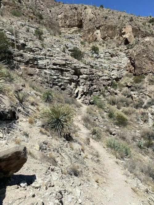 Rocky hillside with sparse vegetation and a narrow dirt path winding through the arid landscape.