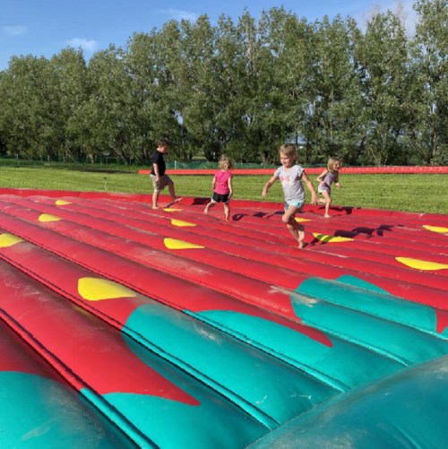 Children playing on a colorful inflatable bouncy surface in a sunny outdoor setting.