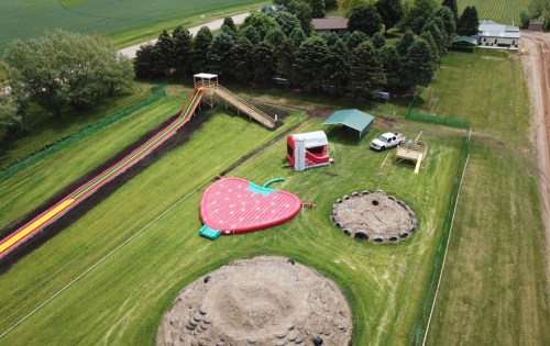 Aerial view of a fun outdoor area featuring a large water slide, inflatable slide, and play structures surrounded by greenery.