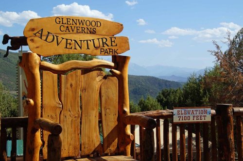Wooden sign for Glenwood Caverns Adventure Park with a large chair and a sign indicating an elevation of 7100 feet.