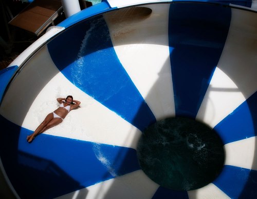 A person relaxes on a blue and white water slide, with water swirling in the center.