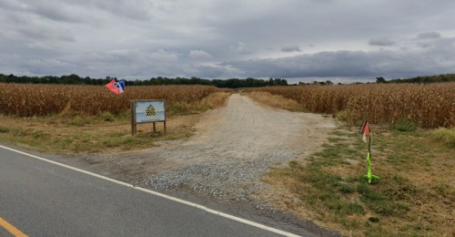 A gravel path leads into a field, with a sign for a zoo and a flag nearby under a cloudy sky.