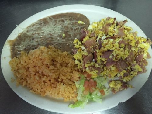 A plate of food featuring scrambled eggs with ham, rice, refried beans, lettuce, and diced tomatoes.