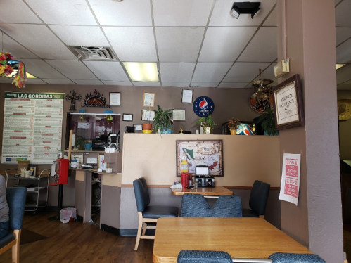 Interior of a casual restaurant featuring wooden tables, a counter with decor, and a menu board on the wall.